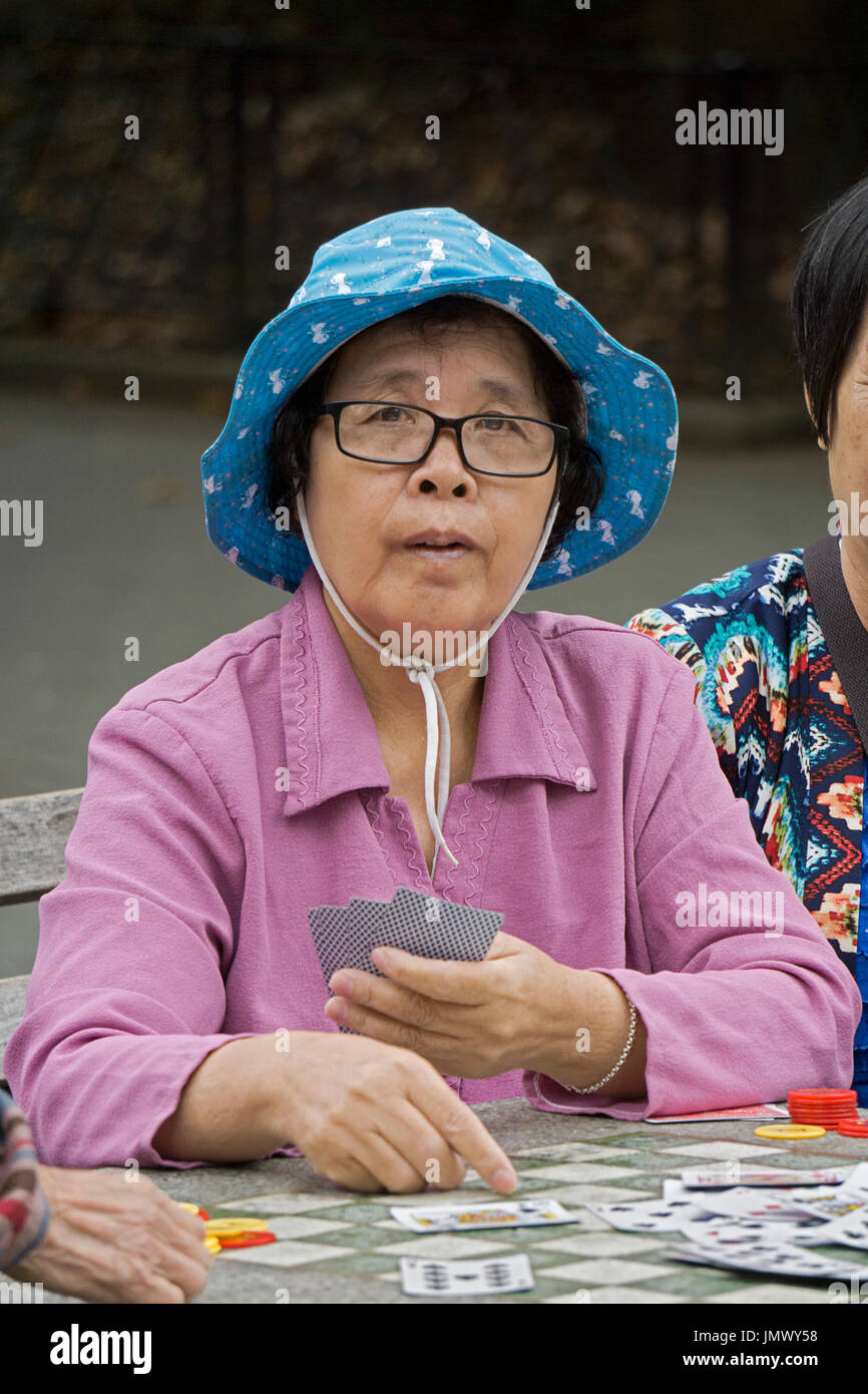 Une vieille femme chinoise à une table pour un jeu de cartes que les femmes dans Columbus Park dans le quartier chinois, la ville de New York. Banque D'Images