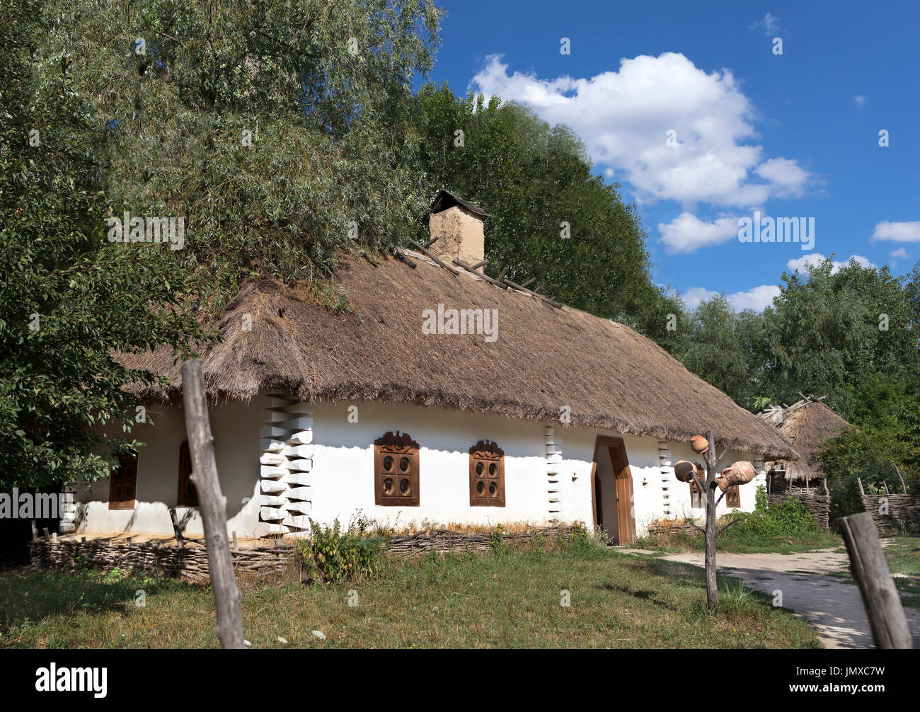 Ancienne maison rurale traditionnelle ukrainienne avec toit de chaume et de barrière dans le jardin contre un ciel bleu avec un nuage blanc Banque D'Images