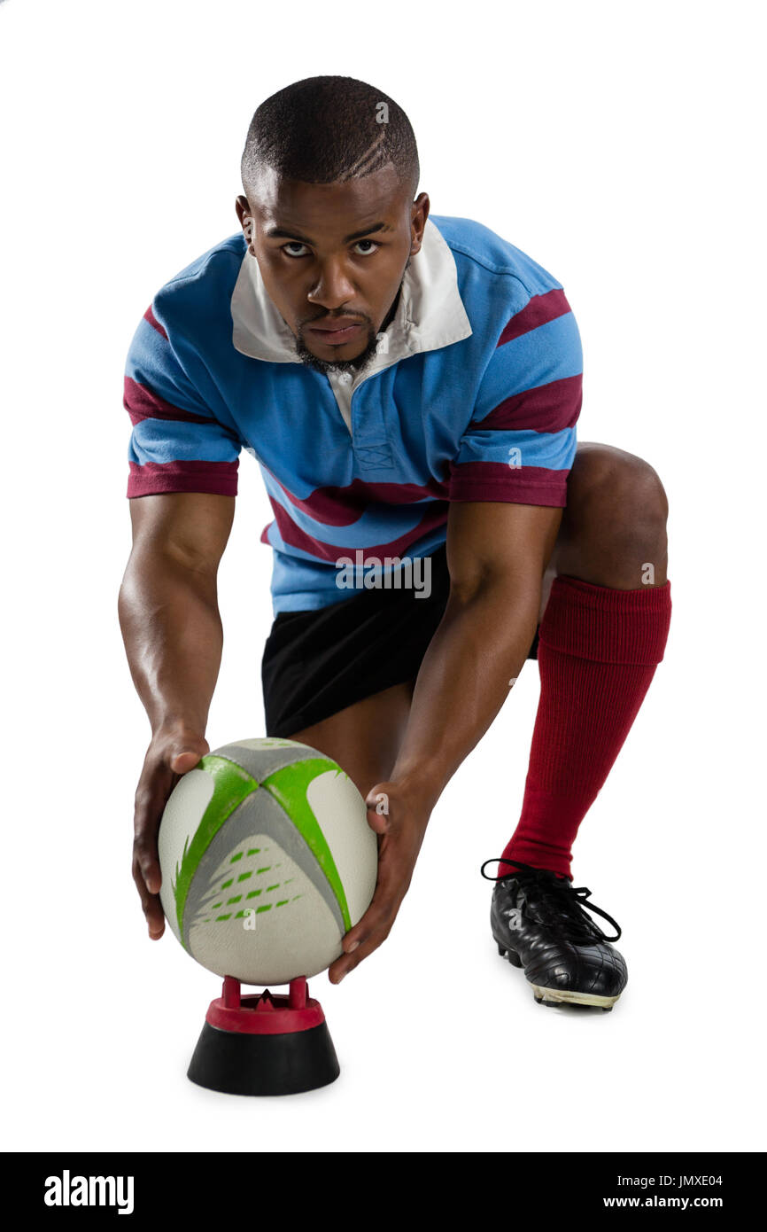 Portrait de l'homme joueur de rugby ball le maintien alors qu'en t'agenouillant contre fond blanc Banque D'Images