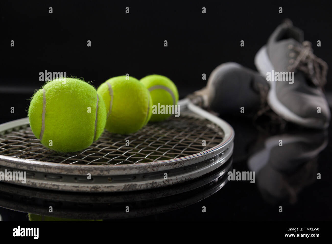 Close up de balles de tennis jaune fluorescent sur racket par des chaussures de sport sur fond noir Banque D'Images