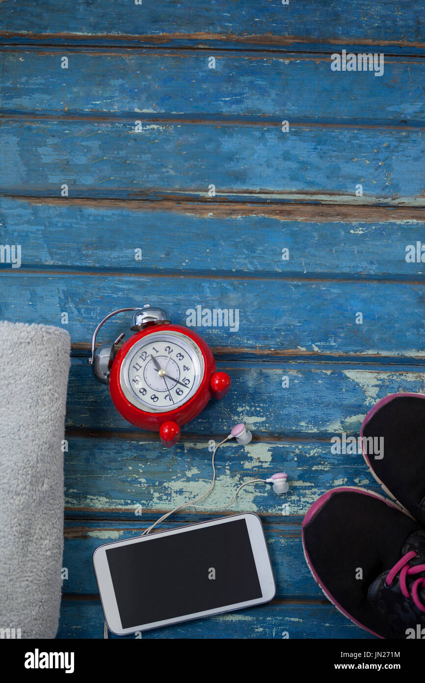 Vue de dessus de réveil par téléphone mobile au milieu de nappes et des chaussures de sports sur table en bois bleu Banque D'Images