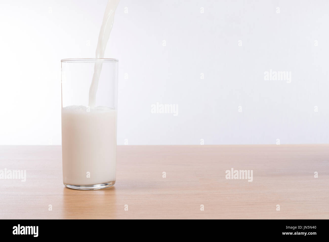 Lait frais et verser dans un verre à moitié plein sur un banc de bois brut haut avec fond blanc et copiez l'espace. Banque D'Images