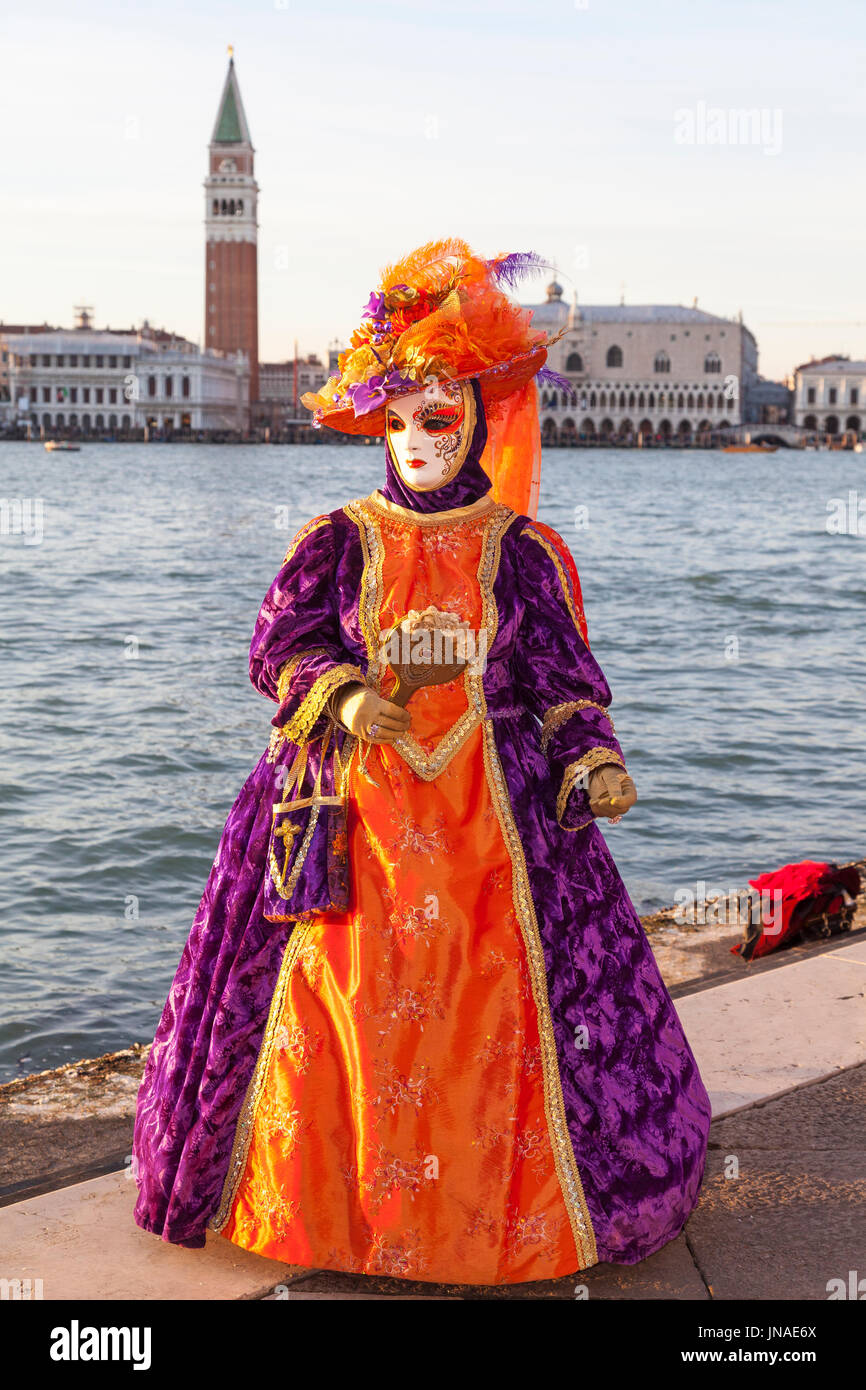 Carnaval de Venise 2017, Venise, Vénétie, Italie. Femme en classique coloré costume orange et violet posant sur San Girogio Maggiore avec les Doges Pal Banque D'Images