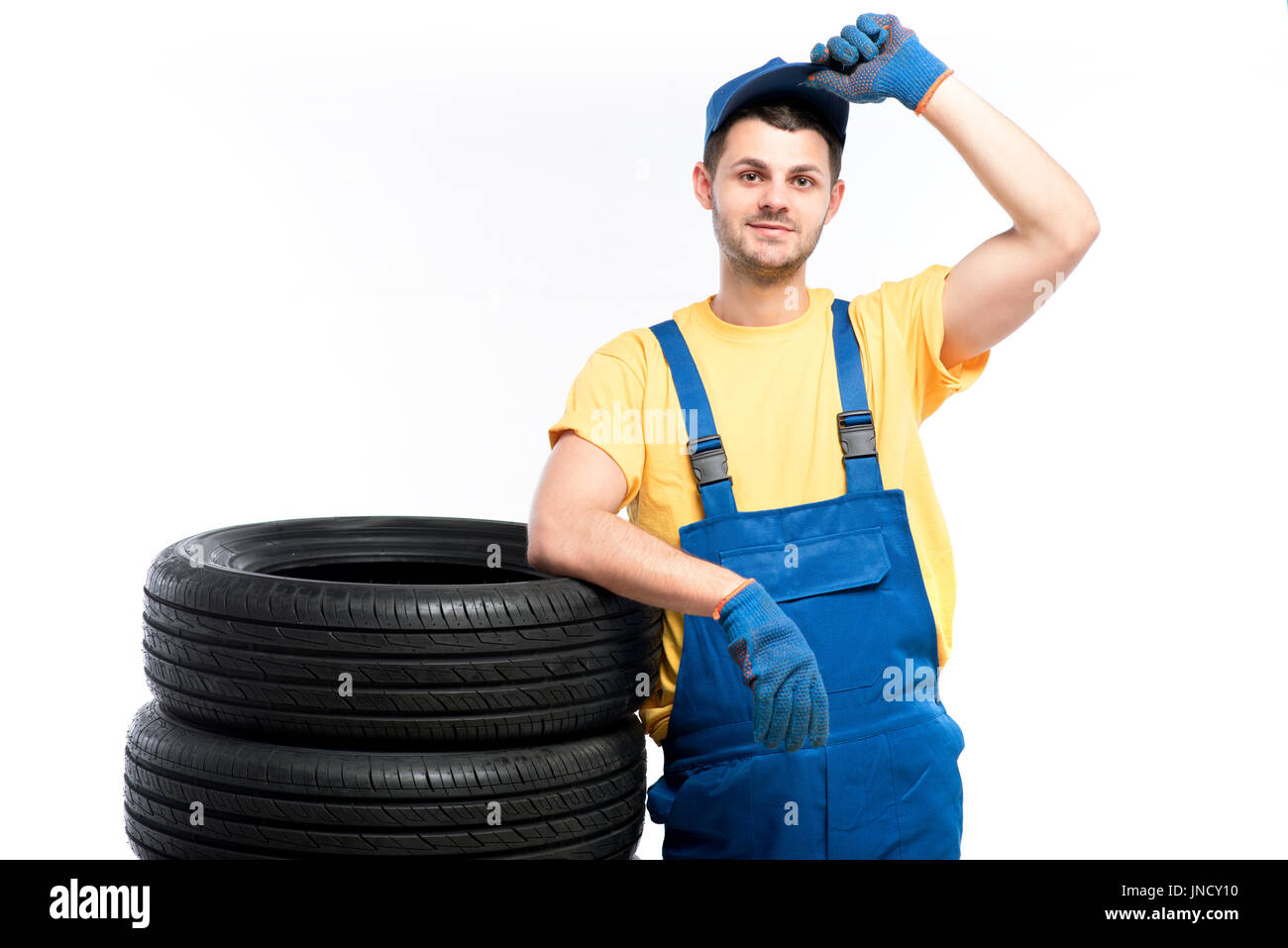 Conscrit dans l'uniforme bleu assis sur pneumatiques, fond blanc, réparateur de pneus Banque D'Images