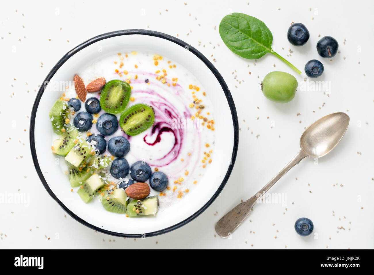 Le Yogourt aux bleuets, le kiwi, les épinards, les amandes, la noix de coco râpée et le pollen d'abeilles dans un bol sur le tableau blanc. Vue d'en haut Banque D'Images