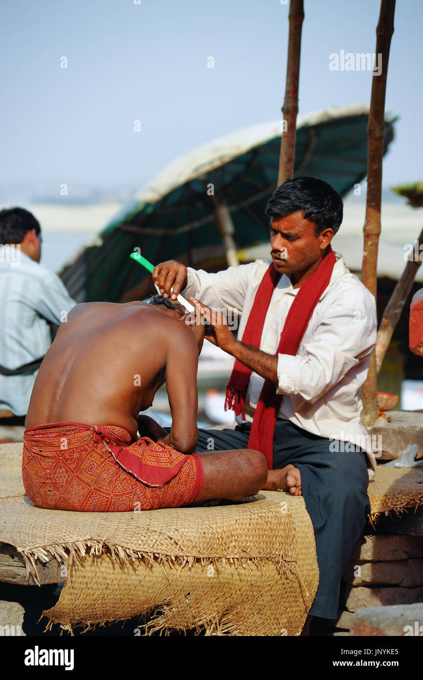Un barbier rase la tête d'un homme sur les rives de la rivière Ganges Banque D'Images