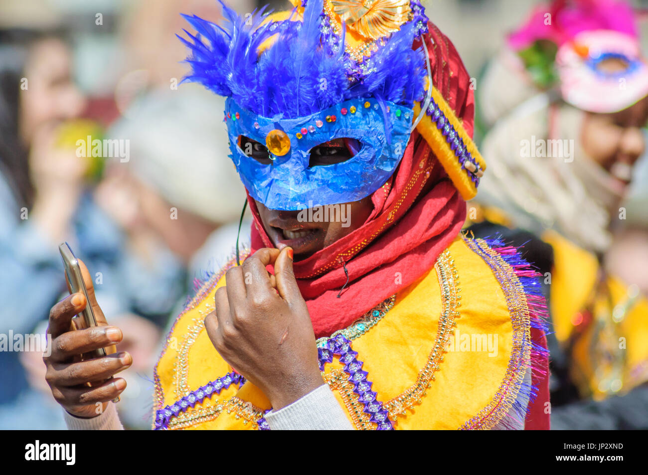 Interprète féminine portant un costume et un masque coloré à l'aide d'un téléphone mobile dans les rues d'Édimbourg dans le carnaval de la Jazz and Blues Festival Banque D'Images