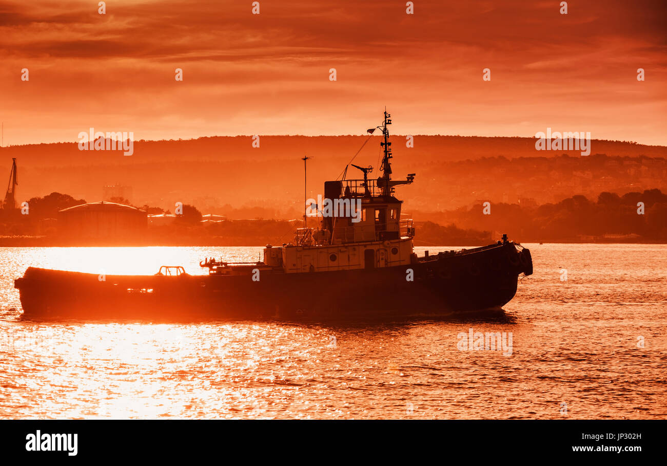 Port de la mer Noire au coucher du soleil. Tug boat est en cours, le port de Varna, Bulgarie. Photo avec des tons de rouge effet lens flare Banque D'Images