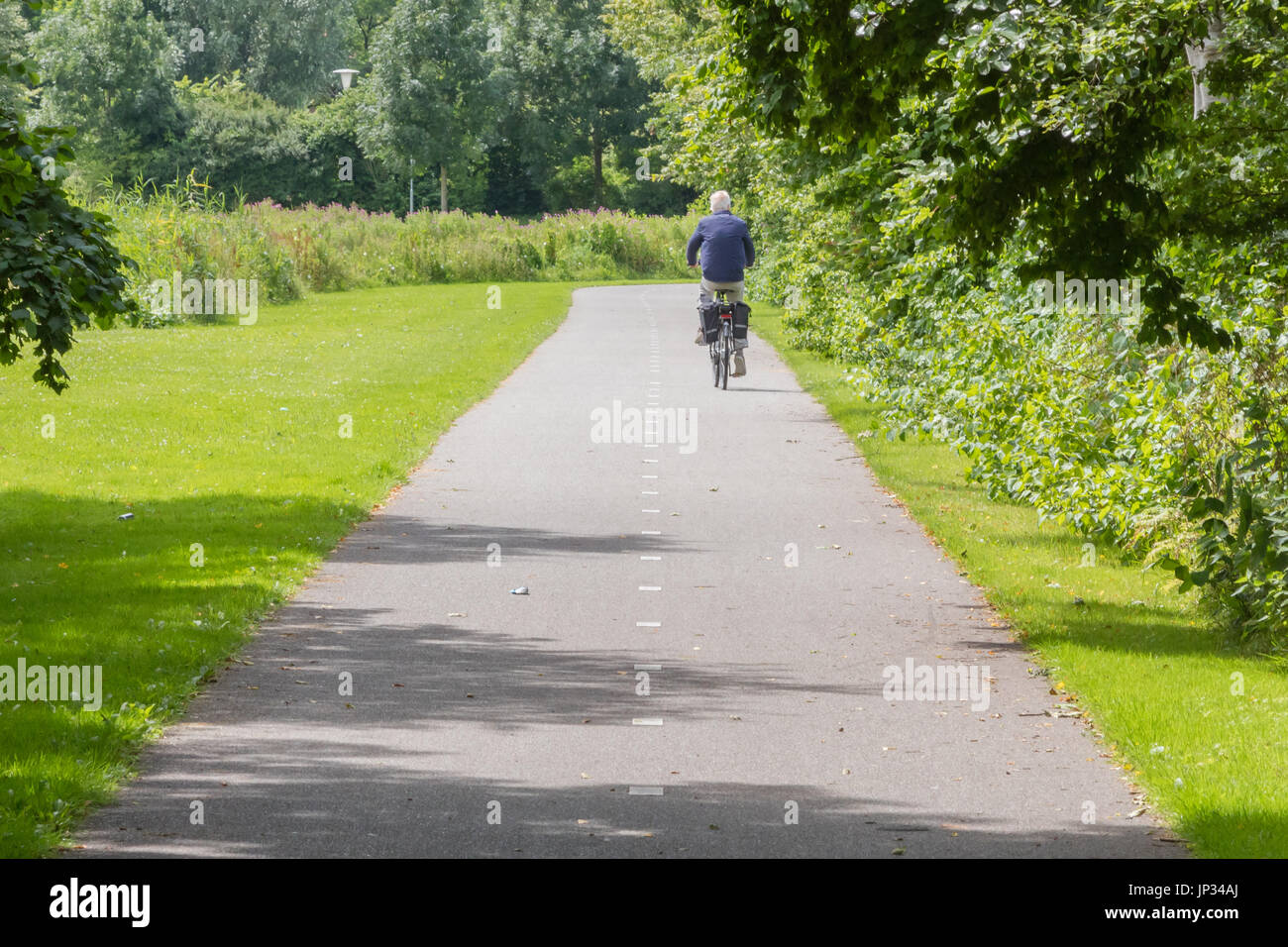 Vieil homme méconnaissable de faire du vélo sur route asphaltée. Banque D'Images