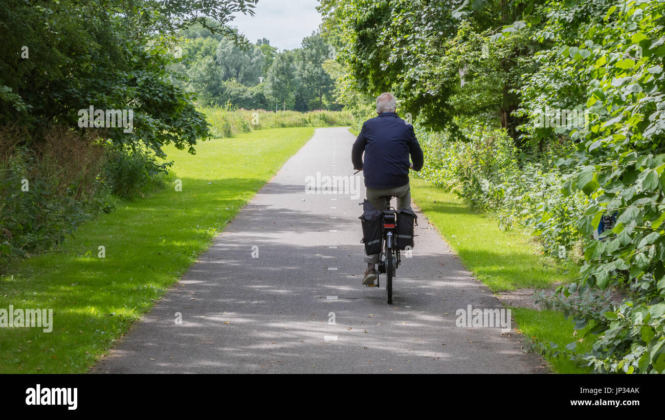 Vieil homme méconnaissable de faire du vélo sur route asphaltée. Banque D'Images