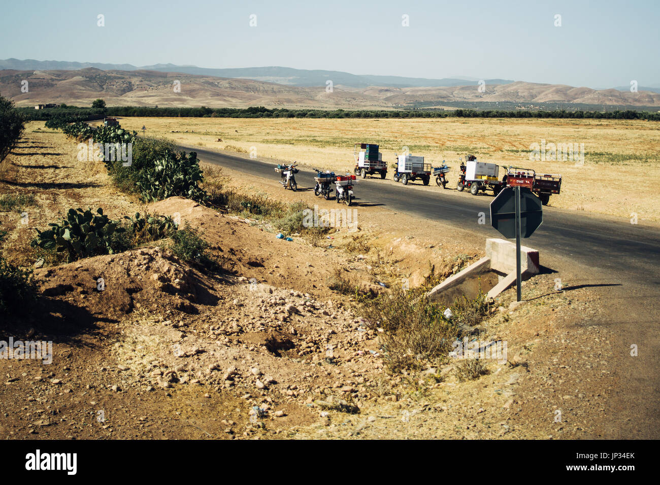 Paysage aride au Maroc avec une rue et les véhicules stationnés à elle. Banque D'Images