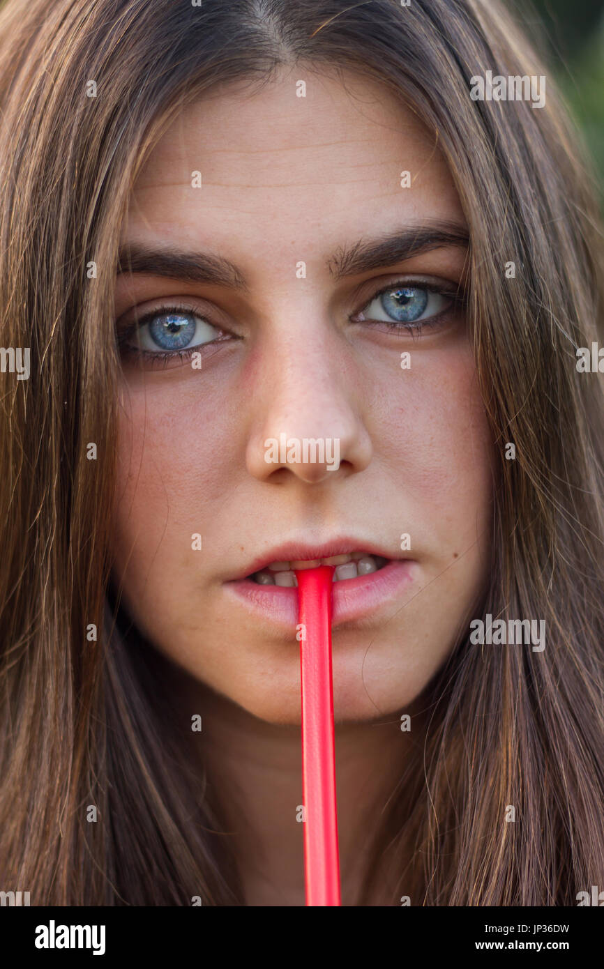 Jeune fille avec des yeux bleus et des cheveux brun rouge de manger de la réglisse. Portrait photo est un gros plan de son visage. Banque D'Images