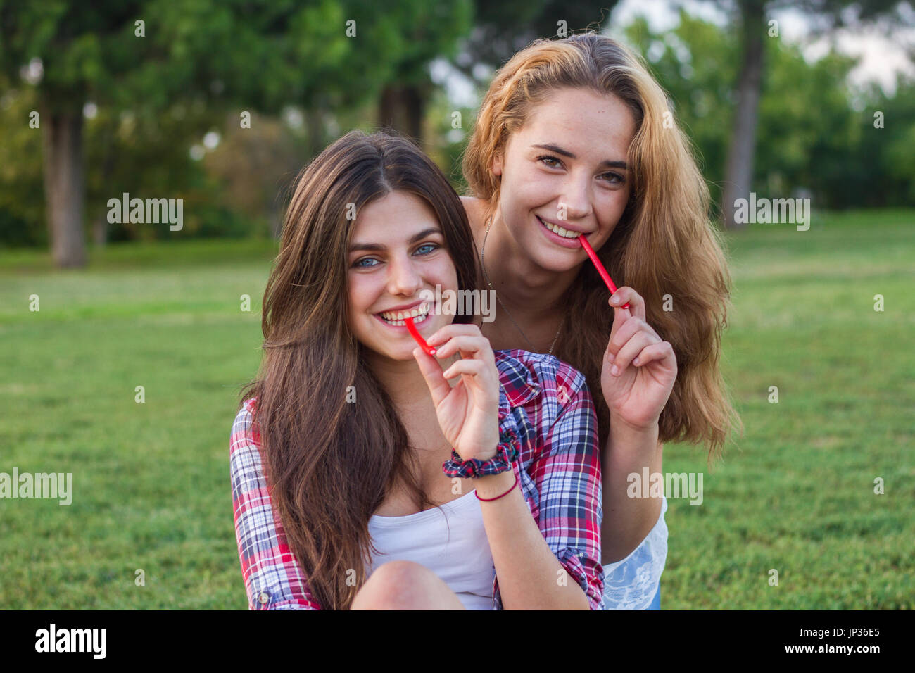 Female friends enjoying en mangeant une réglisse rouge maison de vacances dans le parc. Ils sont jeunes, l'un a les yeux bleus et l'autre est blonde. Banque D'Images