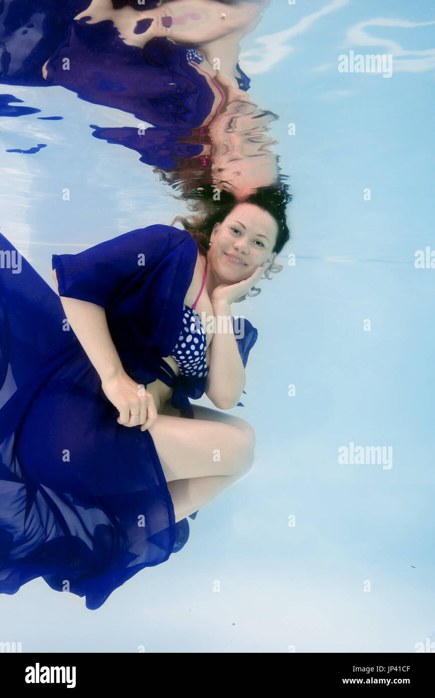 La femme en bleu dress posing sous l'eau dans la piscine Banque D'Images