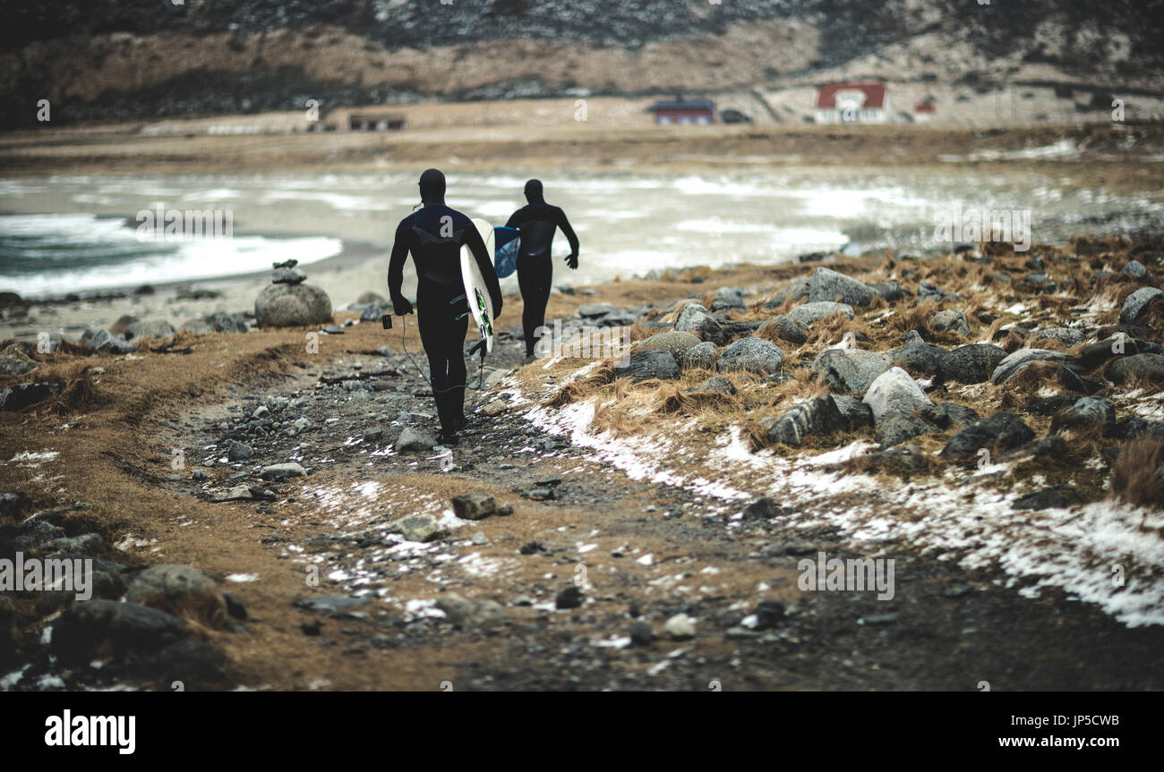 Deux surfeurs portant des combinaisons et l'exécution des planches de marcher le long d'une plage enneigée. Banque D'Images