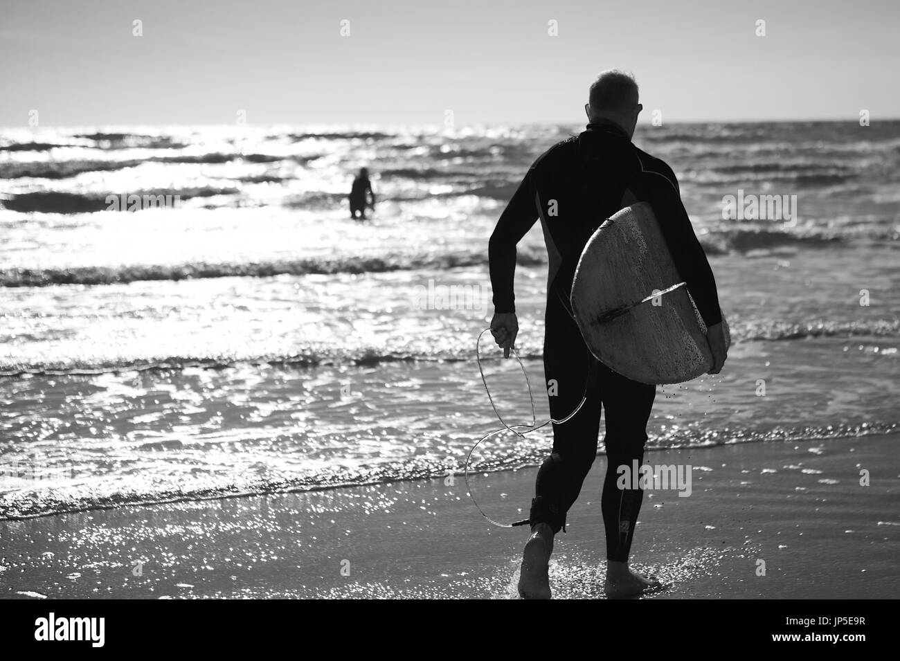 Vue arrière de l'homme en wetsuit standing à l'océan, l'exécution de surf. Banque D'Images