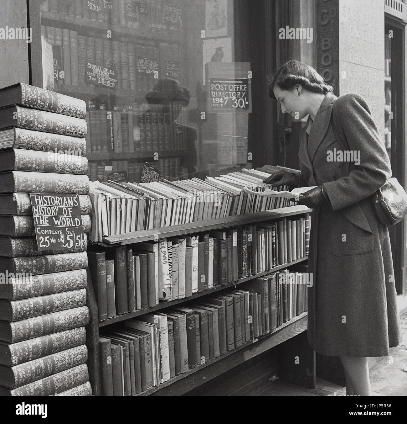 1948, historique, Angleterre, Charing Cross Road, à Londres, une jeune femme parcourt les lignes de la Hardcover Books empilés en dehors d'une librairie de livres anciens. Banque D'Images