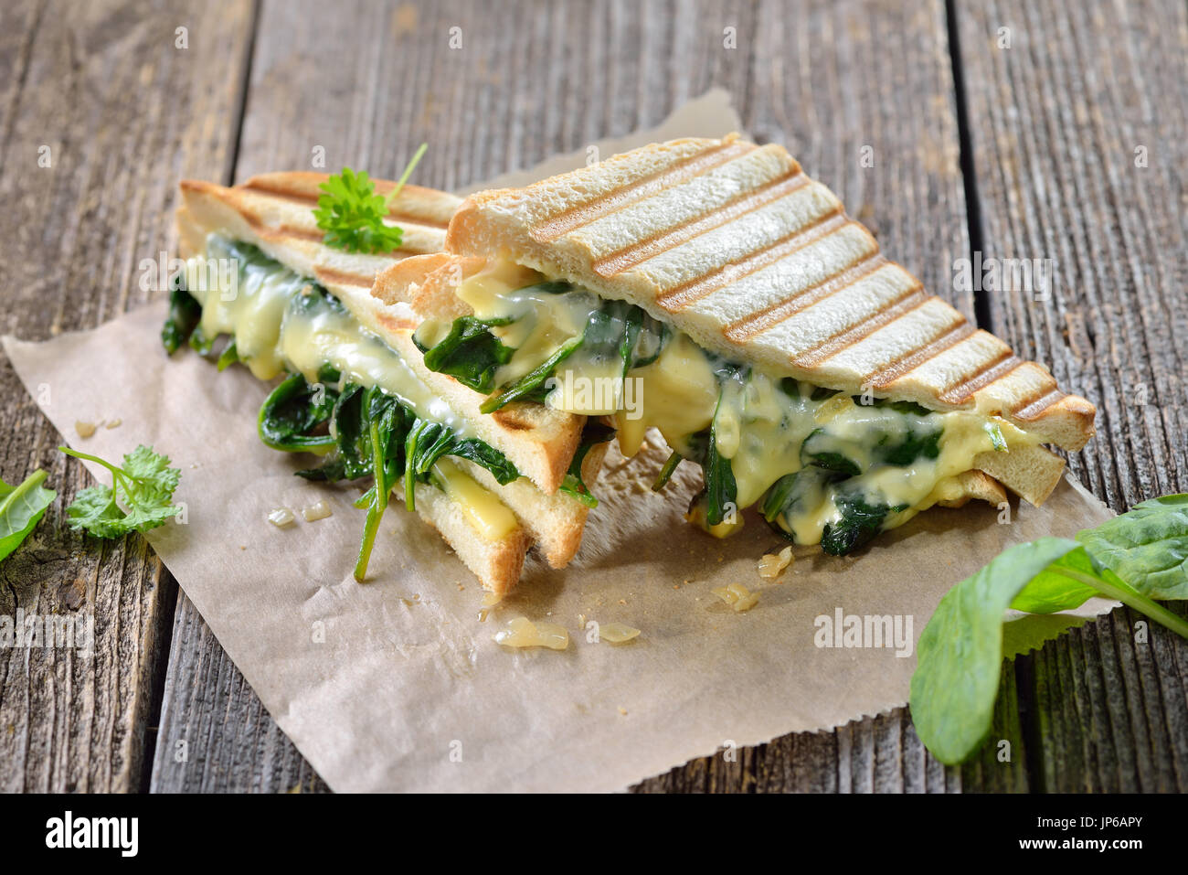 Double appui sur végétarien panini avec de jeunes feuilles d'Épinards, oignons et fromage servi sur du papier sandwich sur une table en bois Banque D'Images