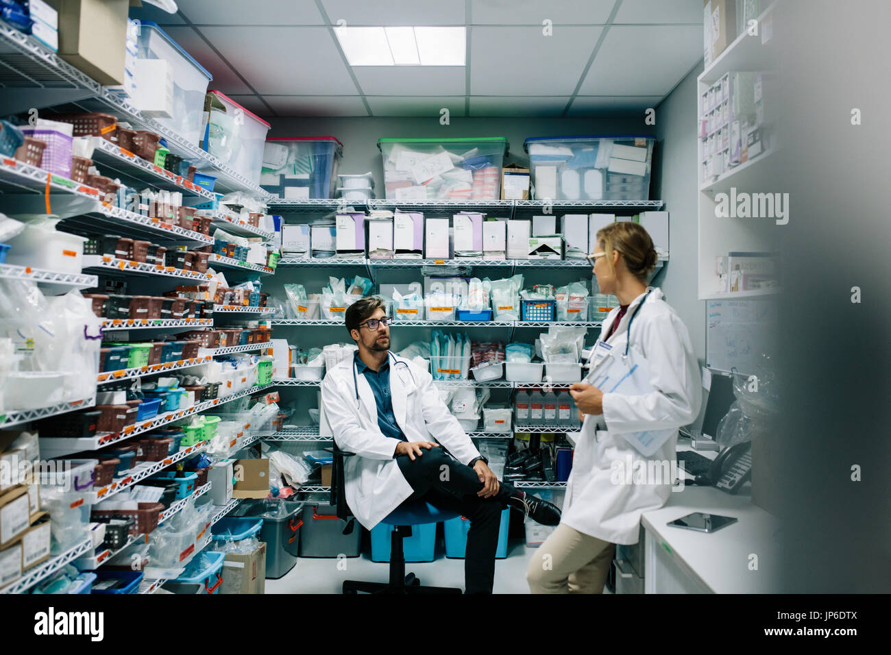 Le personnel de l'hôpital de discuter en pharmacie. Médecin Homme assis avec femme debout et parler. Banque D'Images