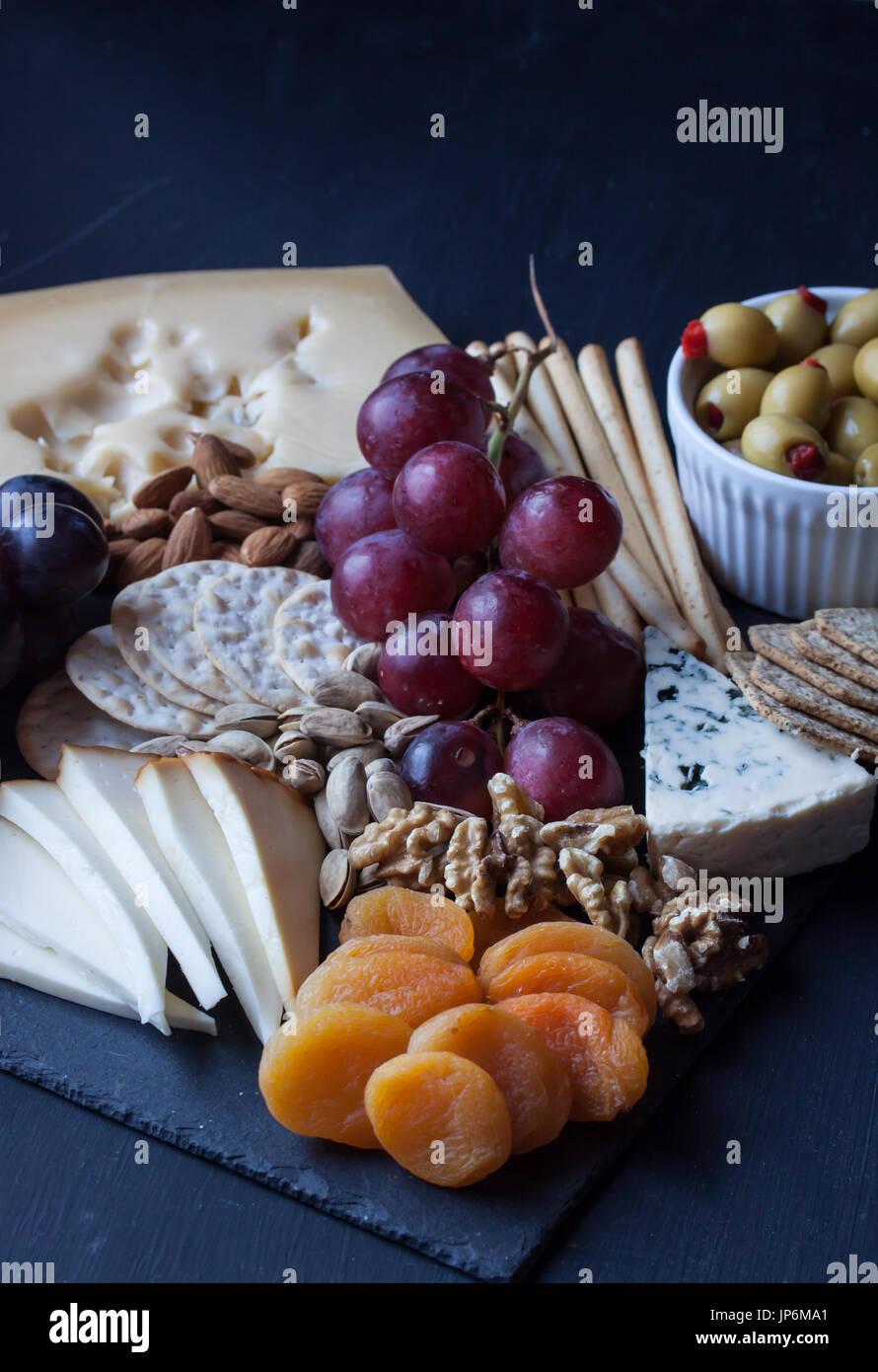 Assortiment de fromages, craquelins, raisins, noix et d'olive sur un fond noir Banque D'Images