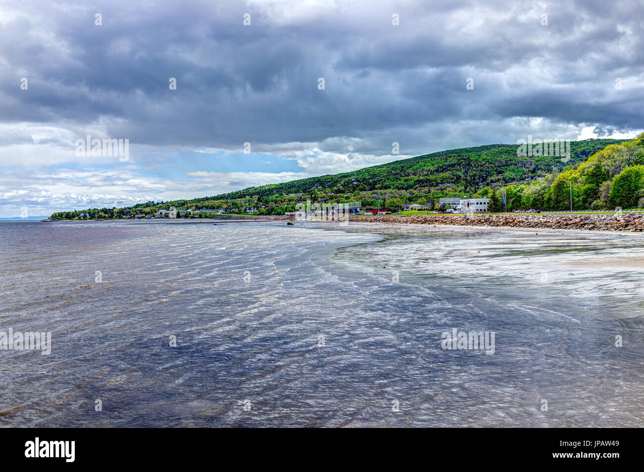 La Malbaie, Canada - 2 juin 2017 : la Saint Lawrence River shore, vagues et nuages orageux avec des toits de la ville et de la route de village ville Banque D'Images