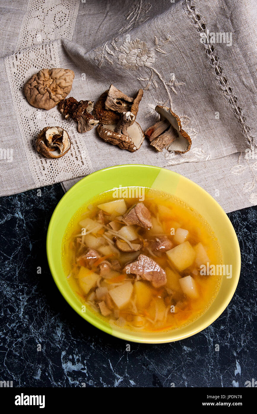 Soupe aux champignons en plaque verte sur un fond noir en noir. Cèpes séchés plusieurs champignons sauvages ou blanc sur tissu marron. Banque D'Images