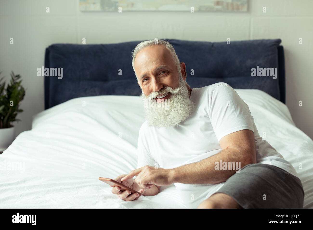 Les barbus man using smartphone alors que lying on bed Banque D'Images