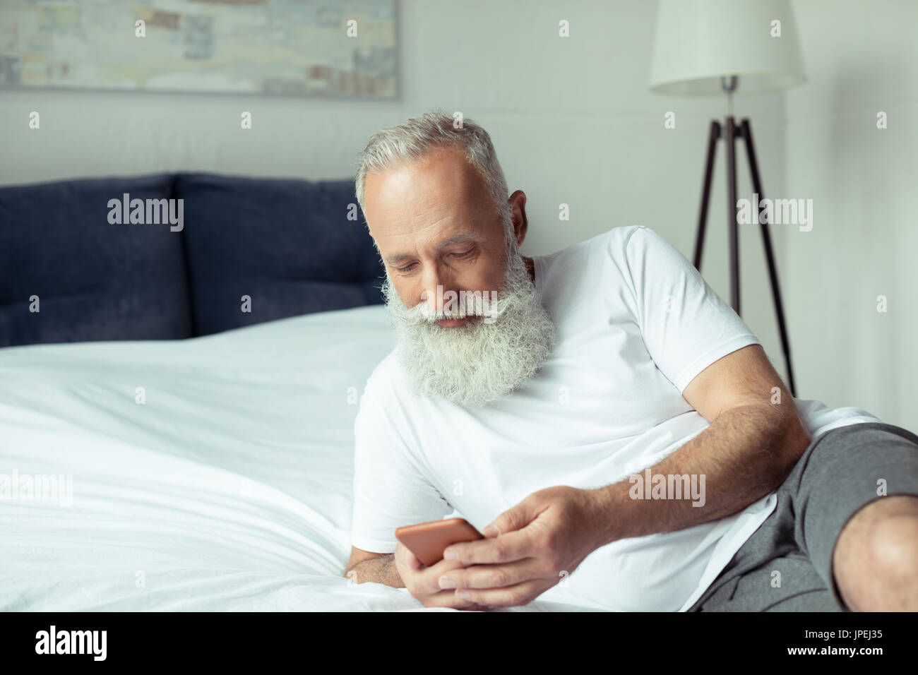 Les barbus man using smartphone alors que lying on bed Banque D'Images