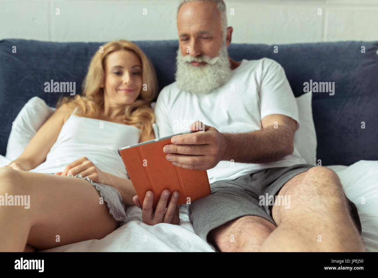 Mature couple using digital tablet while lying on bed at home Banque D'Images