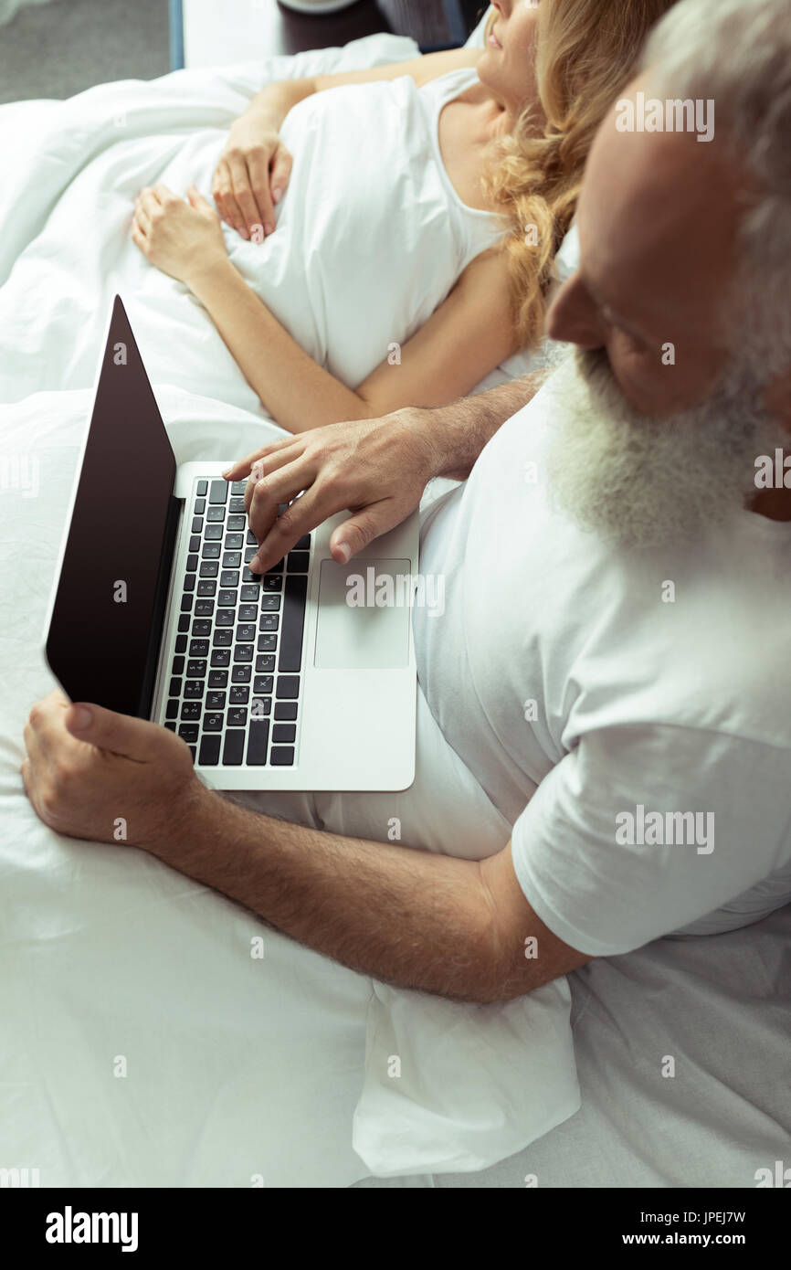 Cropped shot of mature couple resting in bed, man using laptop Banque D'Images