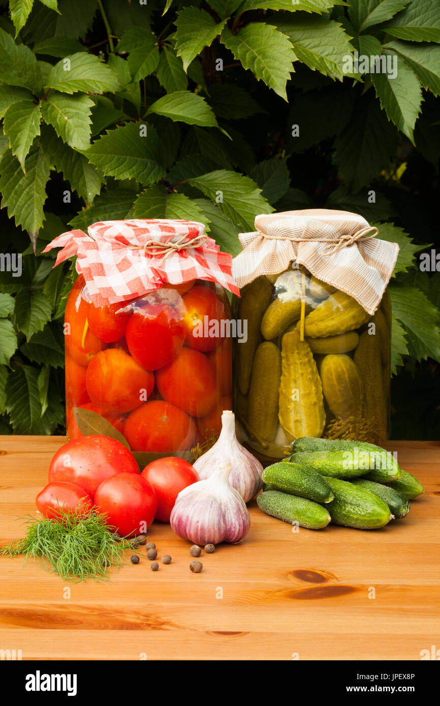 Aliments en conserve et des légumes frais. Conserves de tomates et concombres dans des bocaux en verre sur une table en bois. Des légumes en conserve. Banque D'Images
