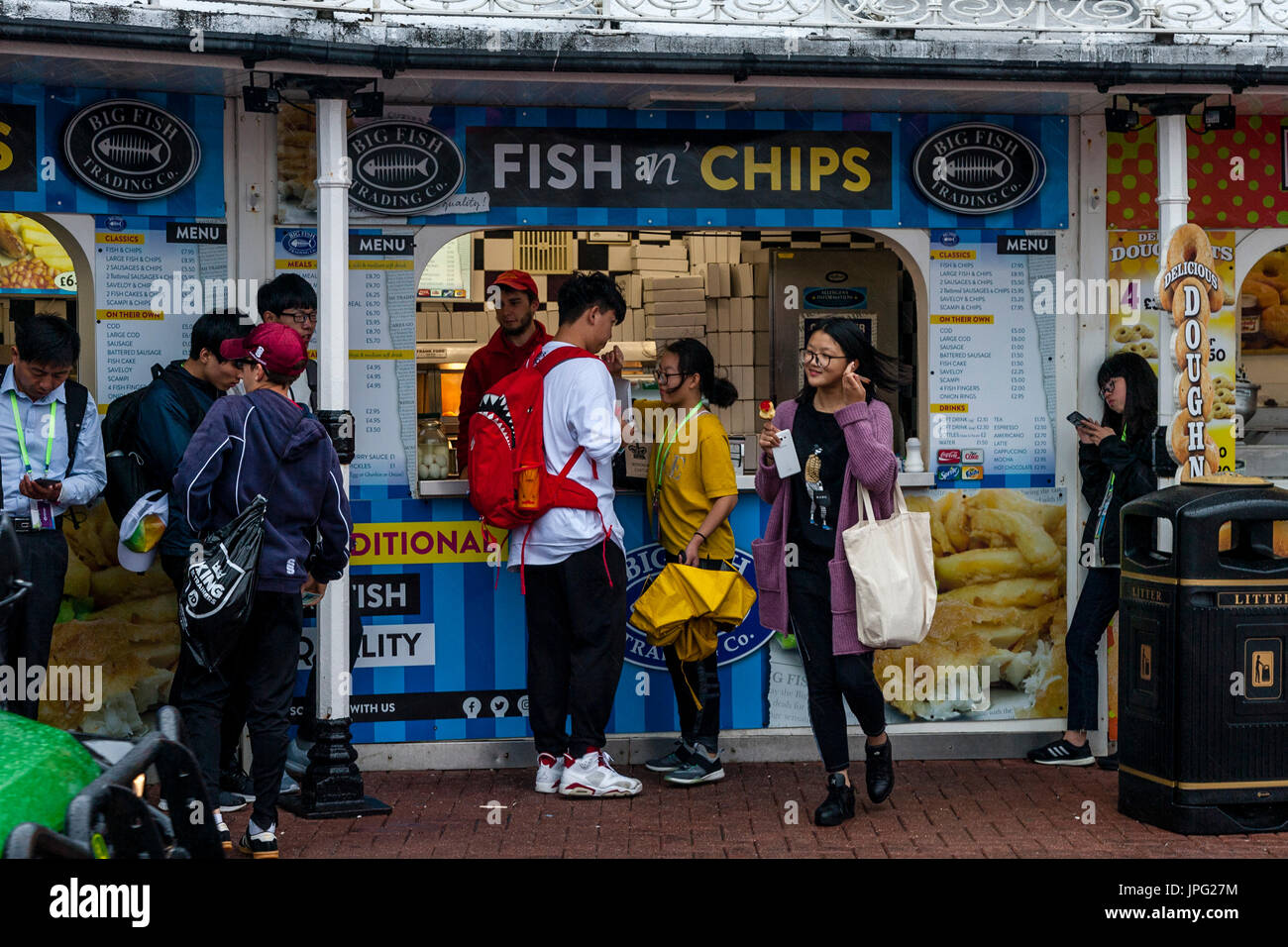 Brighton, UK. 2 Août, 2017. Météo britannique. Un groupe de jeunes touristes chinois d'acheter du poisson et frites sous la pluie sur le front de mer de Brighton, Brighton, East Sussex, UK. Credit : Grant Rooney/Alamy Live News Banque D'Images