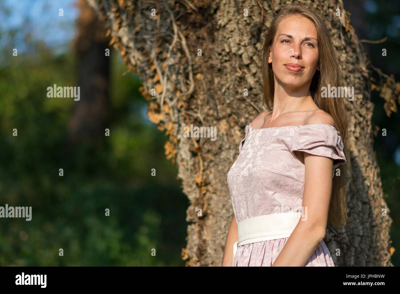 Beau portrait de femme dans une robe rose en face d'un arbre de lierre. Banque D'Images