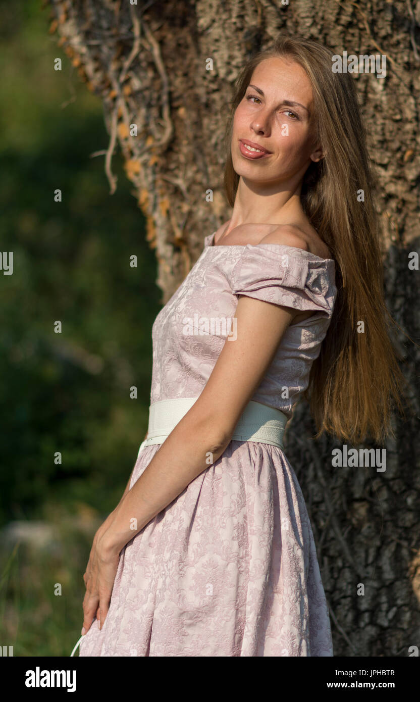 Beau portrait de femme dans une robe rose en face d'un arbre de lierre. Banque D'Images