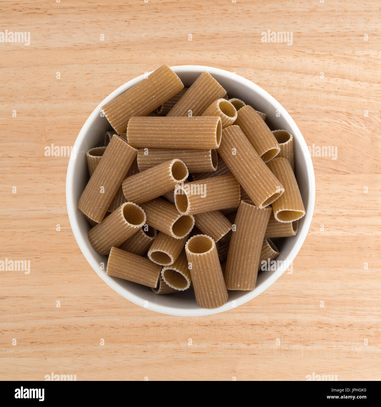 Vue de dessus d'un bol rempli de blé entier en forme de tube pâtes rigatoni sur une table en bois. Banque D'Images