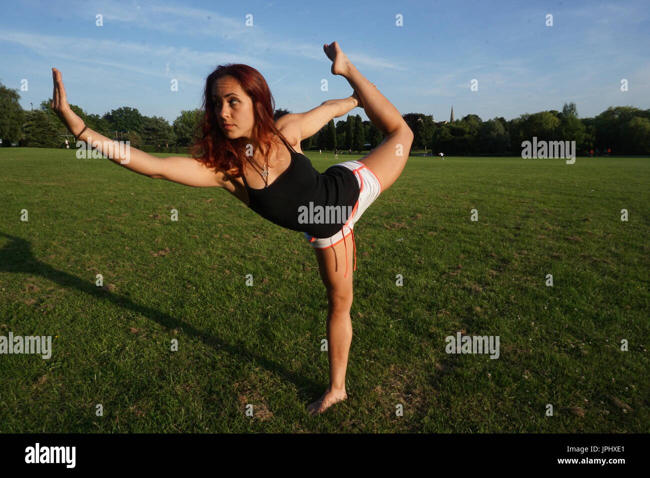Yoga pose à l'extérieur. Longueur pleine vue latérale d'une femme fit pratiquer sur le parc. Le comité permanent arc tirant posent pour la force musculaire et la souplesse. Banque D'Images