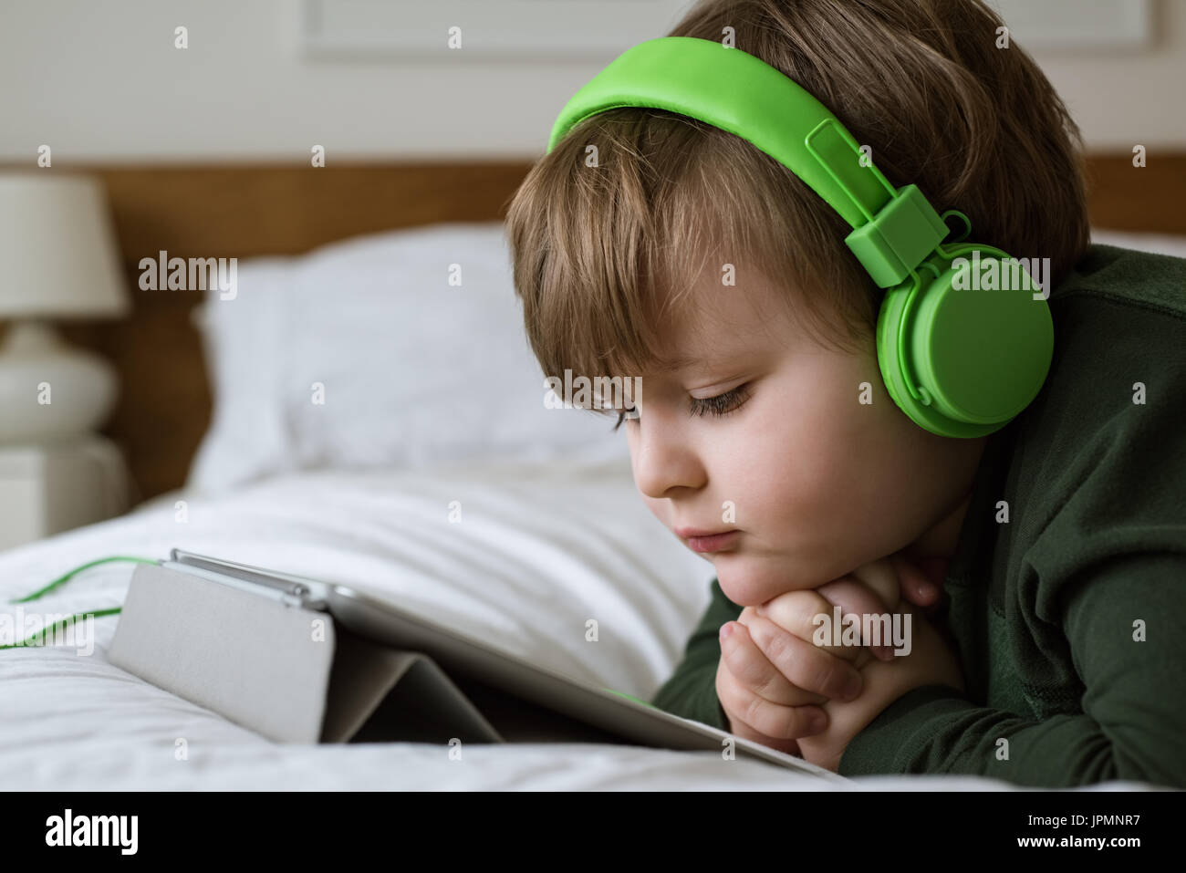 Close up of cute boy portant des écouteurs lors de l'utilisation de digital tablet on bed at home Banque D'Images Close up of cute boy portant des écouteurs lors de l'utilisation de digital tablet on bed at home Banque D'Images