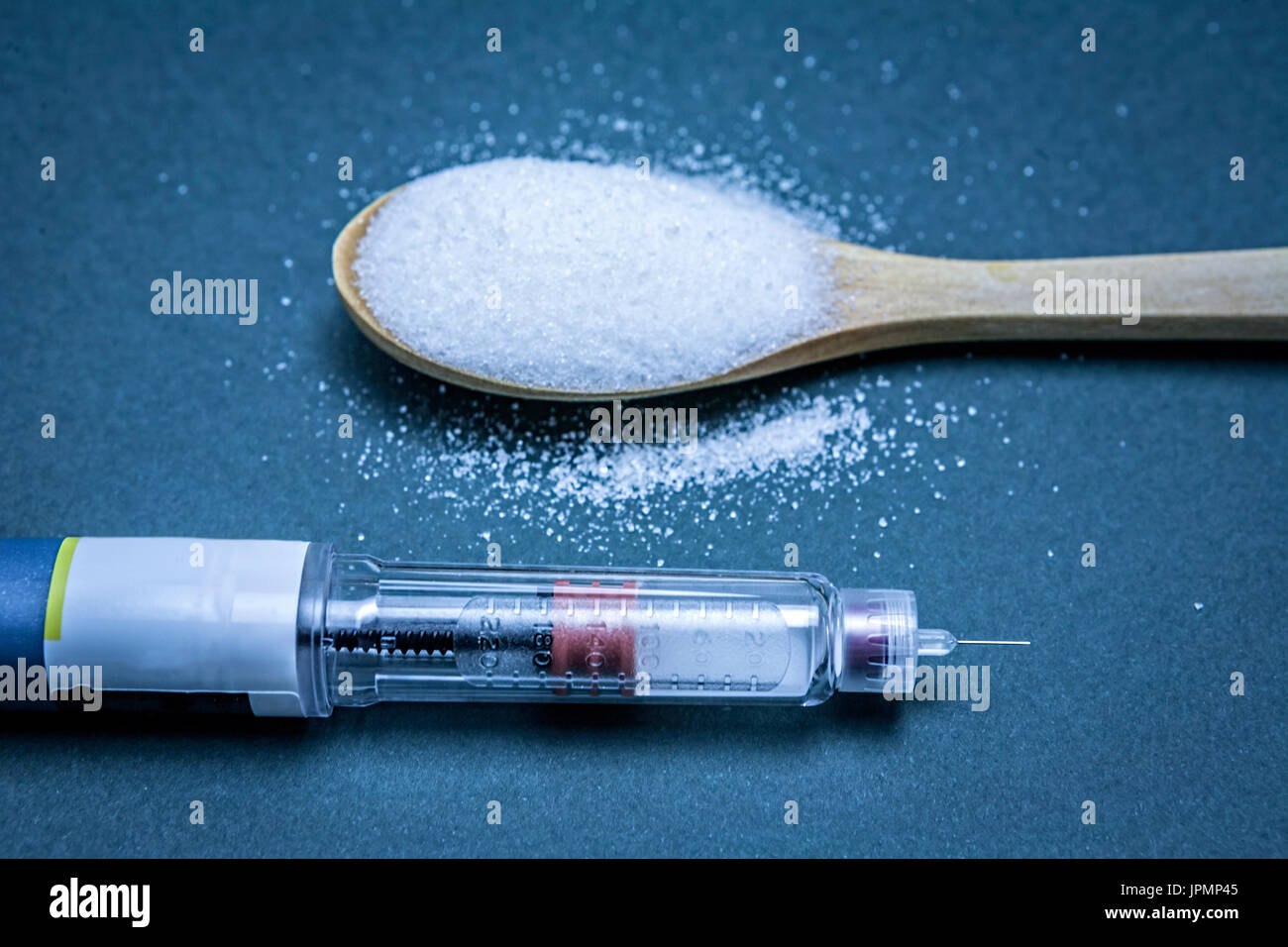 Stylo à insuline ainsi qu'une cuillère à soupe de sucre blanc, de l'hyperglycémie ou de diabète maladie concept sur un fond bleu Banque D'Images