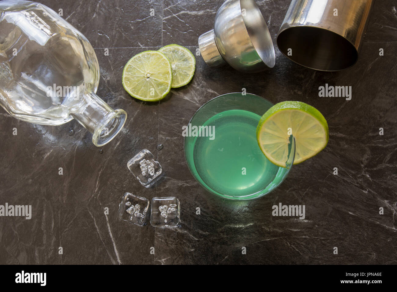 Télévision laïcs de vintage cocktail gimlet gin garni de tranches de citron vert, bouteille de gin, shaker rempli de cubes de glace sur le noir . Banque D'Images