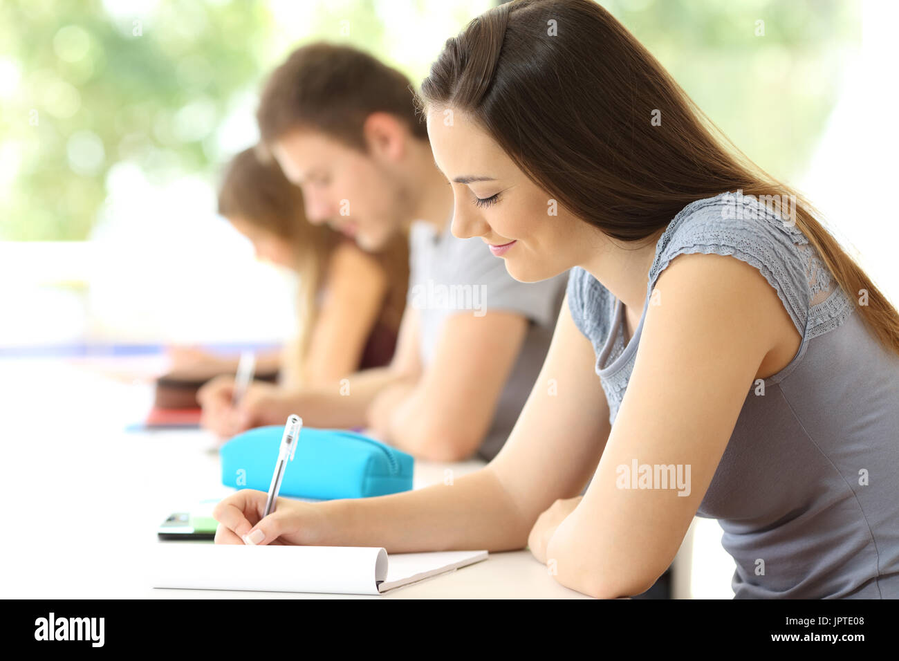 Student taking notes concentrées dans une classe avec des camarades à l'arrière-plan Banque D'Images