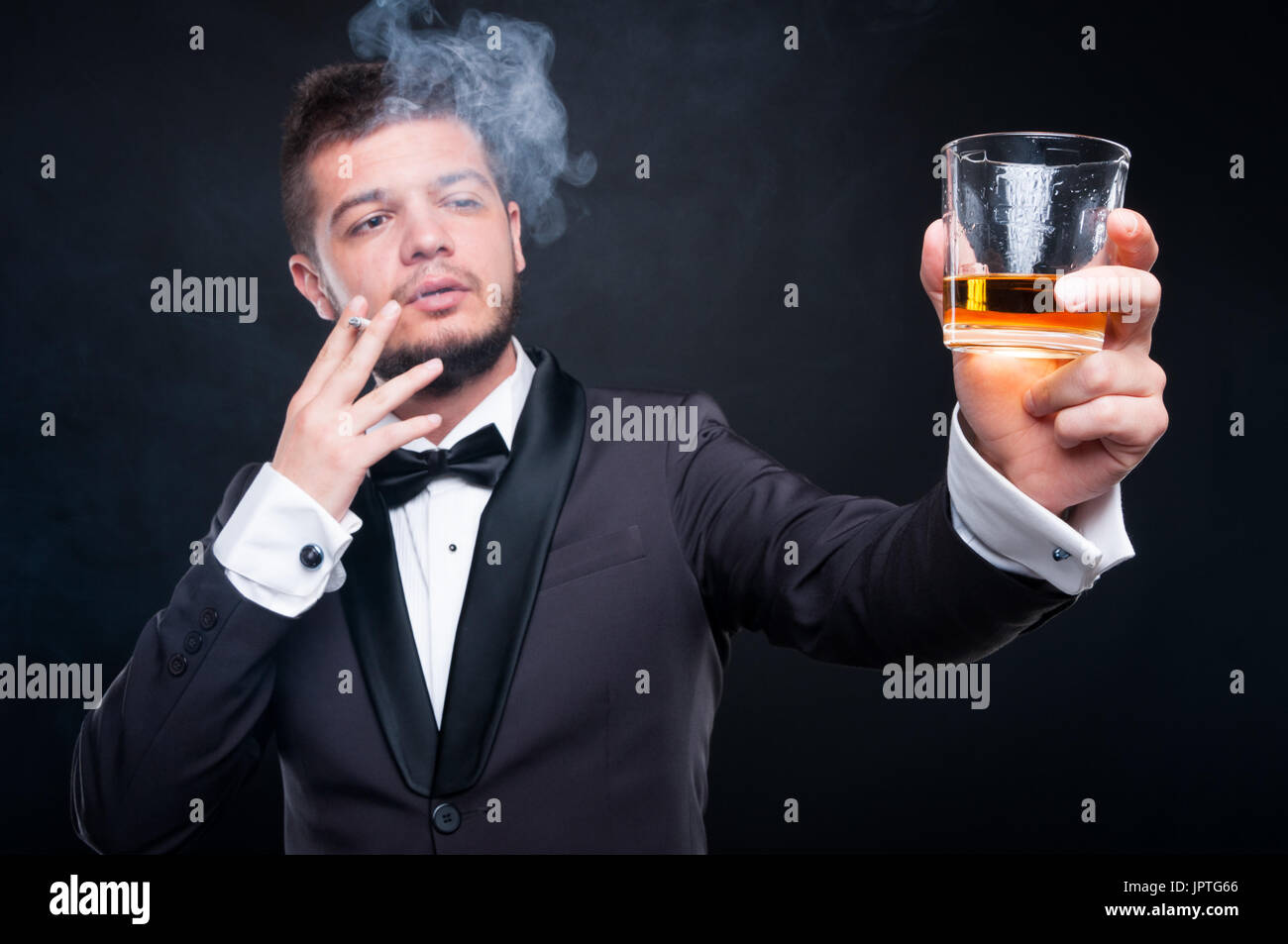 Jeune homme élégant en fonction de l'usage du tabac et d'alcool en verre isolé sur fond sombre Banque D'Images