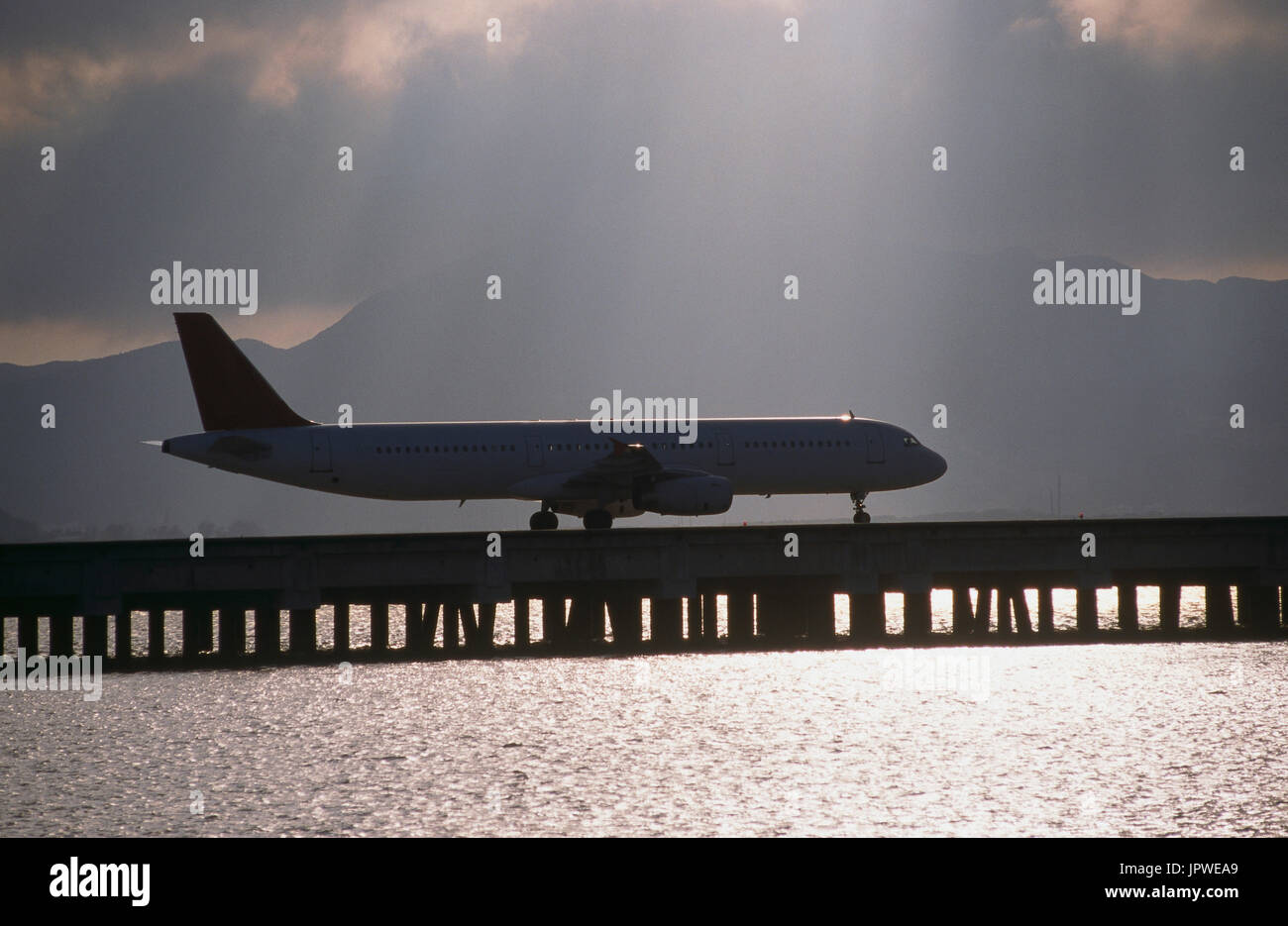 Airbus A321-100 taxiing générique à travers la voie de circulation du pont-jetée sur la mer avec les arbres de la lumière du soleil, soleil étincelant hors de l'eau et les nuages derrière Banque D'Images