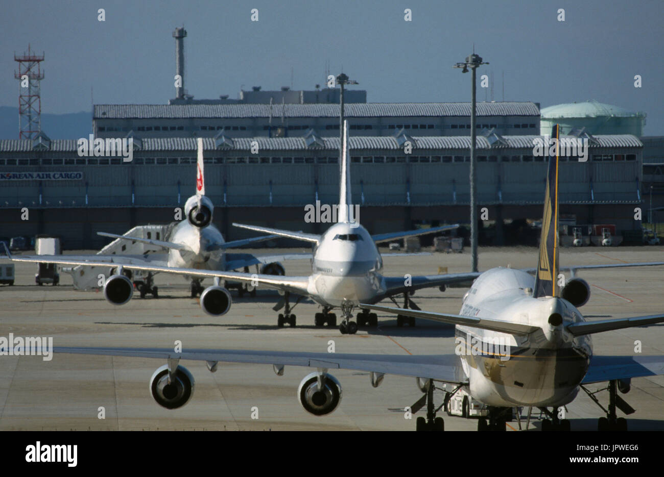Boeing 747-400 de Singapore Airlines soit poussé en arrière par un remorqueur avec un Boeing 747-400 de JAL roulage et McDonnell Douglas DC-10-40 garé au terminal b Banque D'Images
