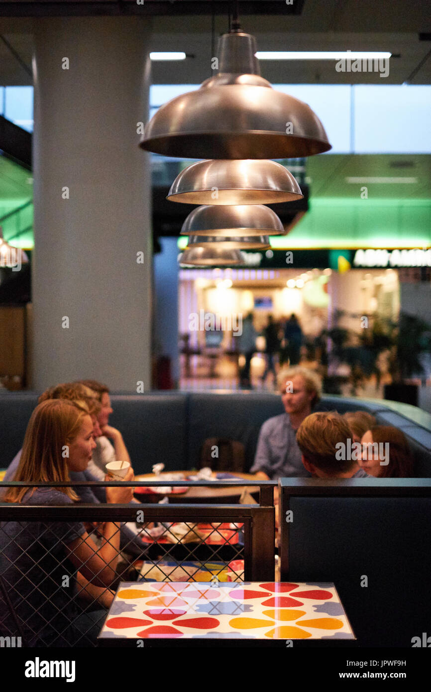 Un groupe de jeunes adultes s'asseoir dans un café à l'aéroport de manger et prendre ensemble. Banque D'Images