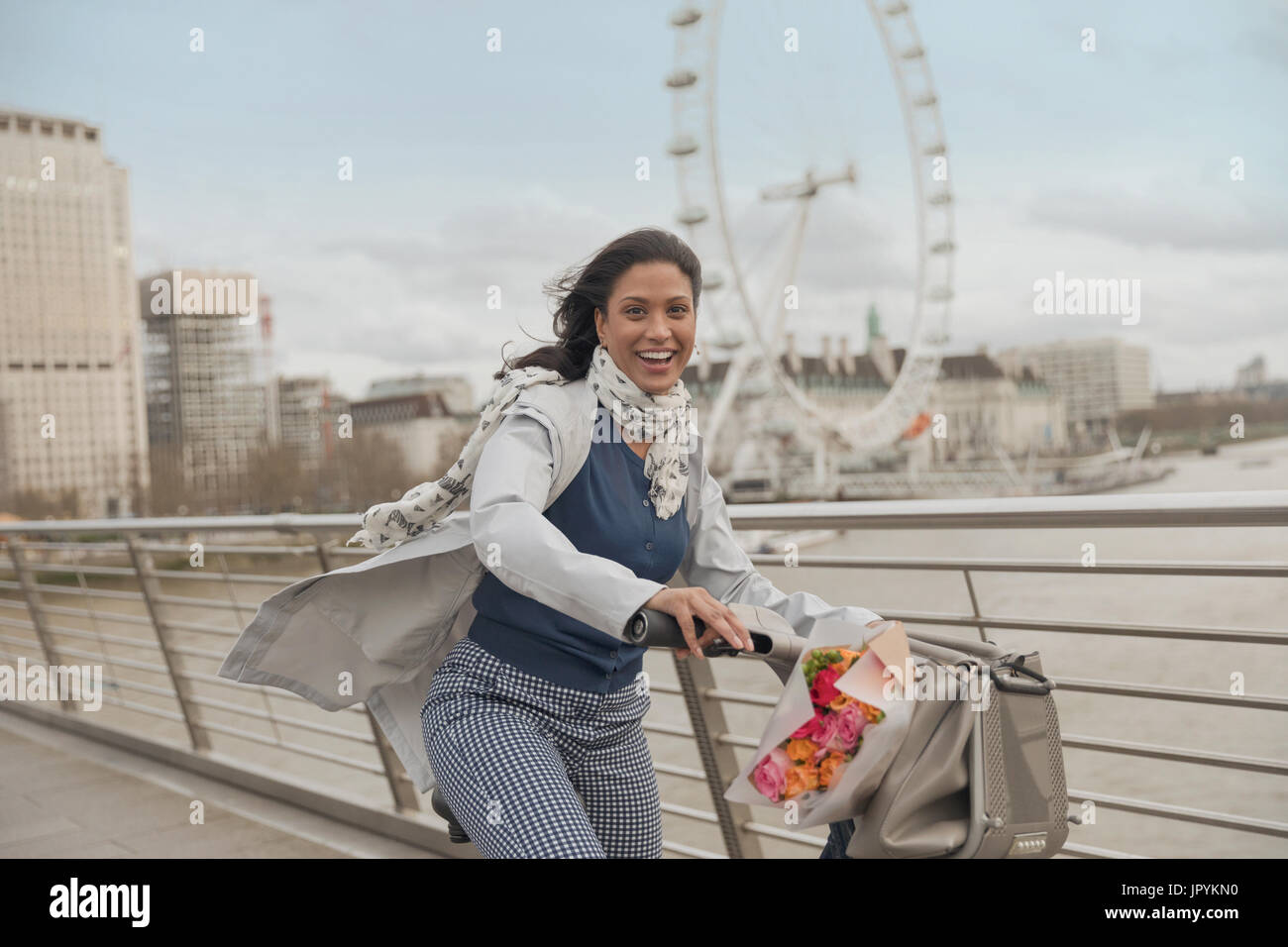Portrait of smiling woman vélo sur pont sur la rivière Thames, près de roue du millénaire, London, UK Banque D'Images