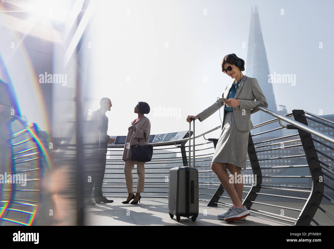 Businesswoman with suitcase écoutez de la musique avec des écouteurs et smart phone, London, UK Banque D'Images Businesswoman with suitcase écoutez de la musique avec des écouteurs et smart phone, London, UK Banque D'Images