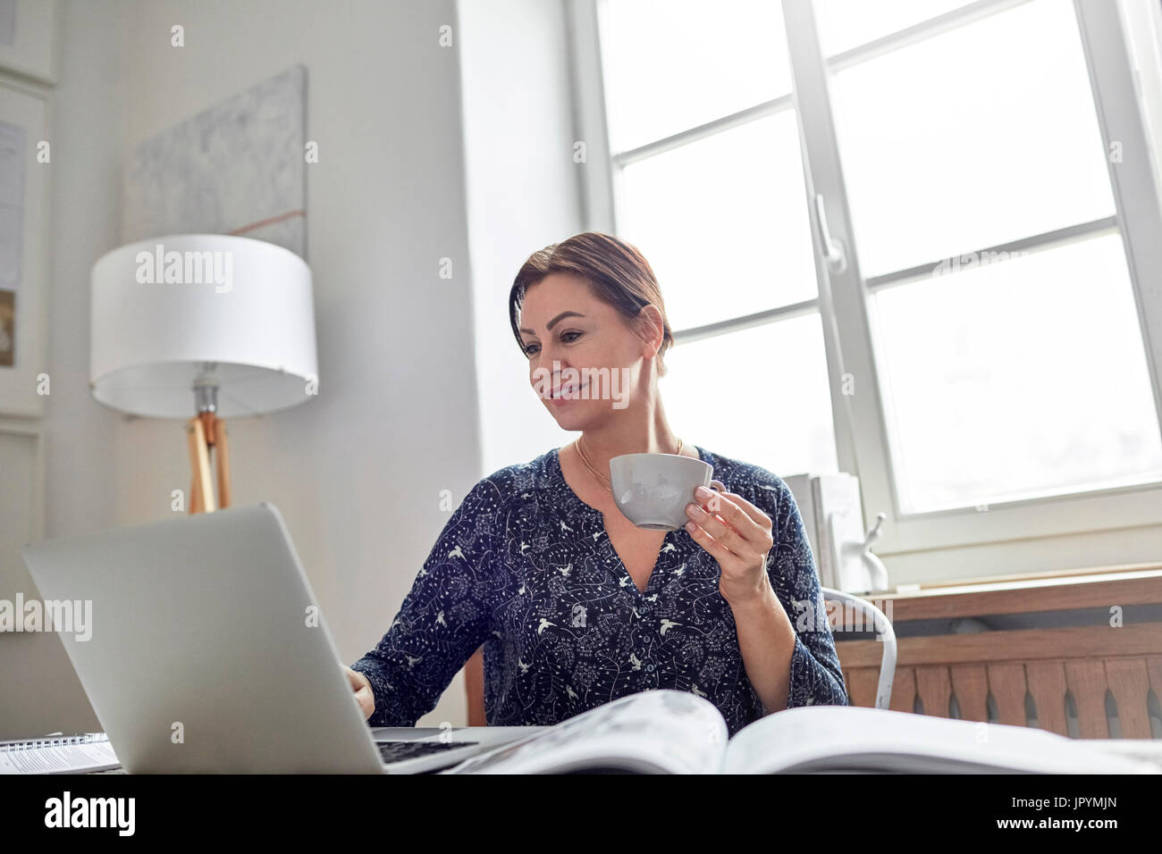 Smiling businesswoman drinking coffee and working at laptop Banque D'Images