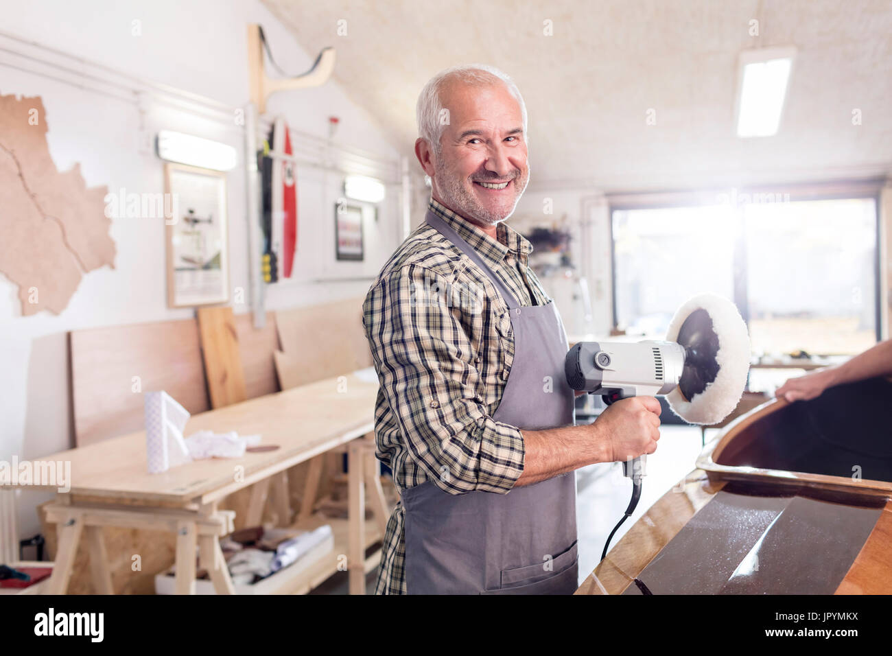 Portrait souriant, confiant senior male carpenter en utilisant un tampon sander sur bateau en bois dans l'atelier Banque D'Images