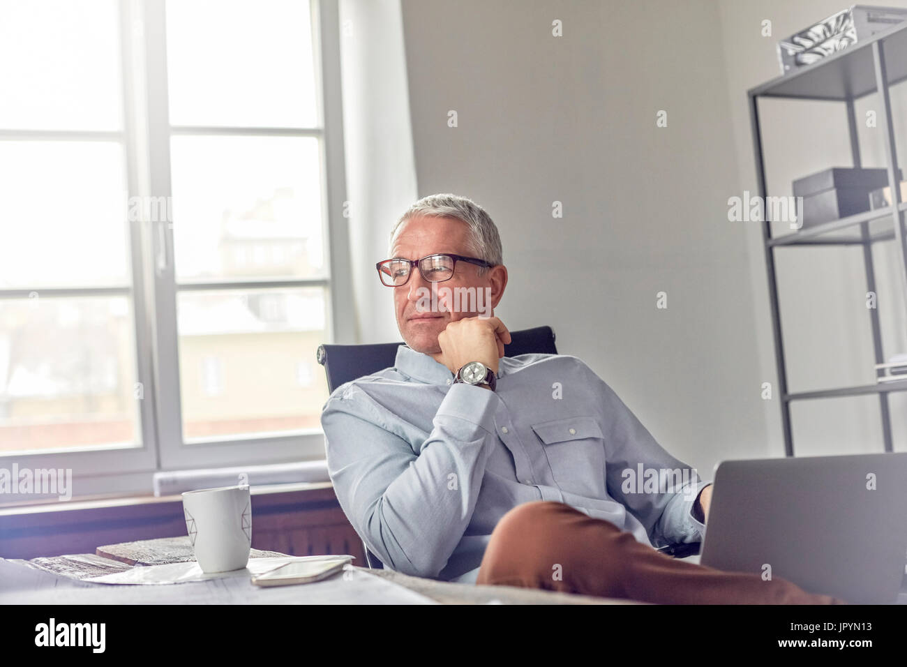 Confiant, pensive businessman with laptop sitting in office Banque D'Images