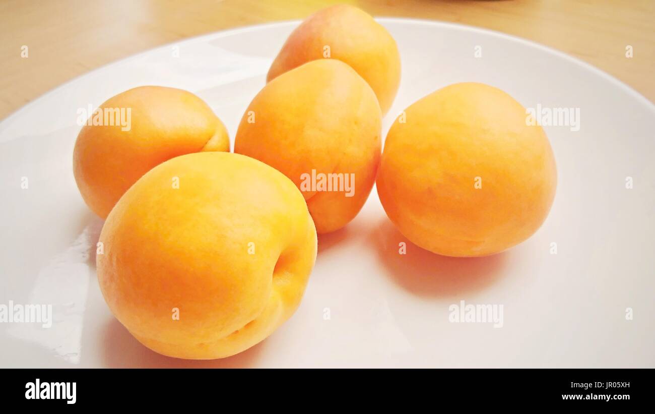 Groupe de cinq abricots sur une plaque blanche. Banque D'Images